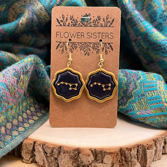 A pair of gold lined polymer clay earrings with a black center and gold dots representing the big dipper